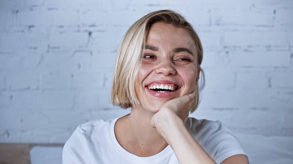 excited woman looking away while laughing in bedroom
