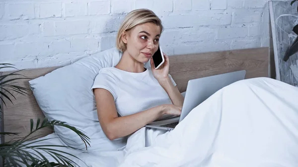 Freelancer Sorrindo Falando Smartphone Enquanto Usa Laptop Quarto — Fotografia de Stock