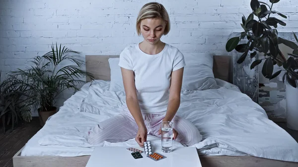Kranke Frau Sitzt Auf Bett Neben Tabletten Und Glas Wasser — Stockfoto