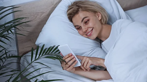 Mulher Loira Feliz Conversando Smartphone Enquanto Deitado Cama — Fotografia de Stock