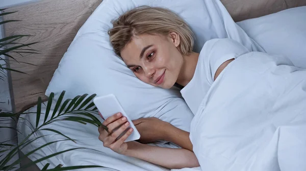Lächelnde Blonde Frau Die Bett Auf Dem Handy Nachrichten Sendet — Stockfoto