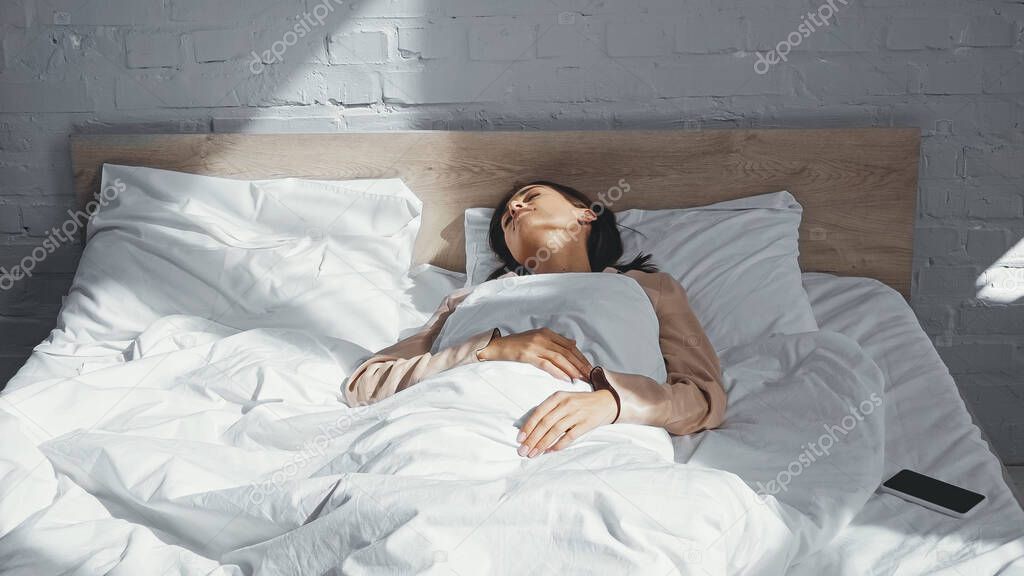 young woman sleeping near smartphone with blank screen