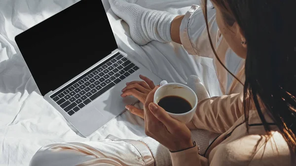 女性在笔记本电脑旁边拿着一杯咖啡 床上有空白屏风的高视角画面 — 图库照片