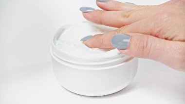 cropped view of woman applying cosmetic cream from container on white clipart