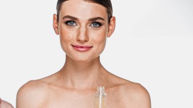 positive woman with naked shoulders and makeup near glass bottle with serum isolated on white clipart