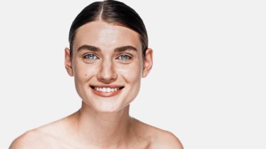 Temiz yüzlü neşeli genç kadın beyaz kameraya bakıyor.