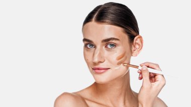 Young adult woman applying different shades of concealer on cheek isolated on white clipart