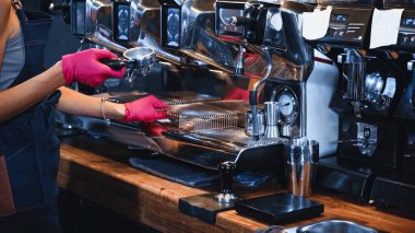 Kahve makinesinin yanında baristanın portafilter tutarken çekilmiş görüntüsü. 