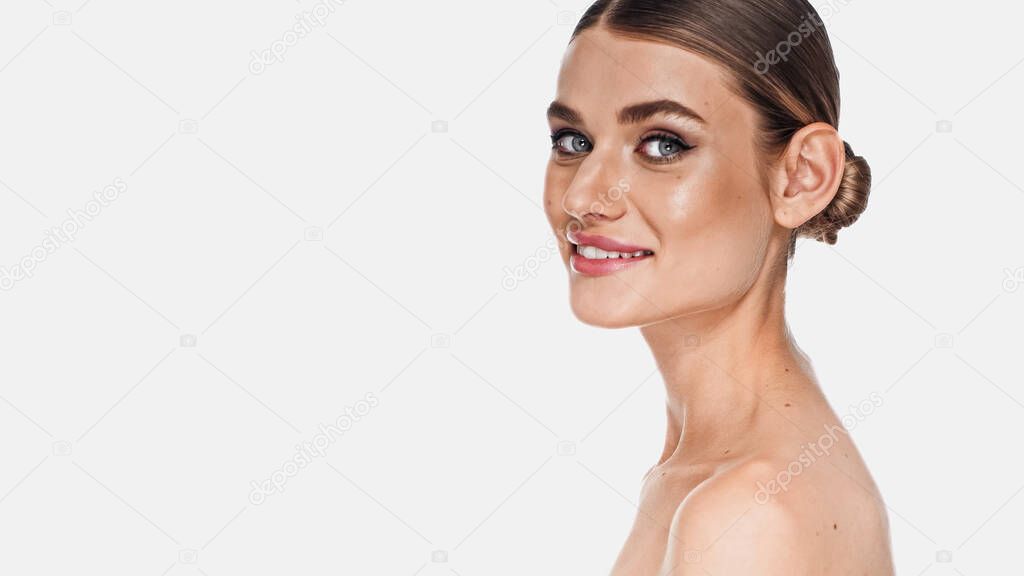 cheerful woman with naked shoulders and makeup looking at camera isolated on white