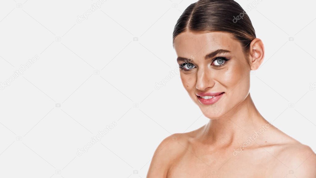 positive woman with naked shoulders and makeup looking at camera isolated on white