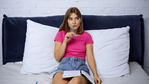 Pensivo Jovem Segurando Caneta Perto Notebook Enquanto Descansa Quarto — Fotografia de Stock