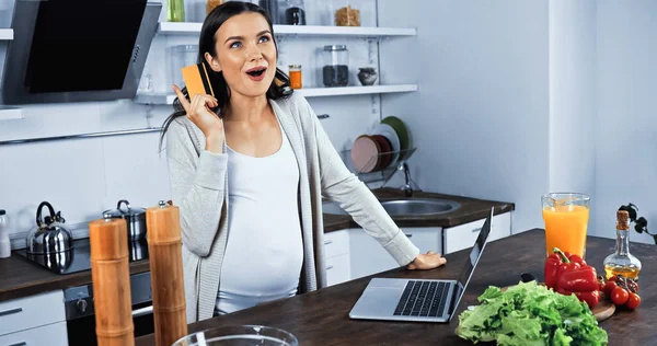 Mulher Grávida Animado Segurando Cartão Crédito Perto Laptop Comida Cozinha — Fotografia de Stock