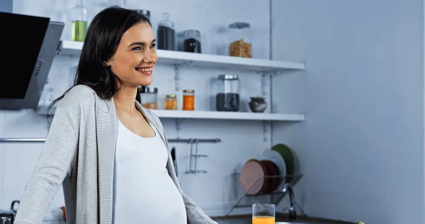 Mujer Embarazada Sonriente Mirando Lejos Cerca Del Jugo Naranja Cocina — Foto de Stock