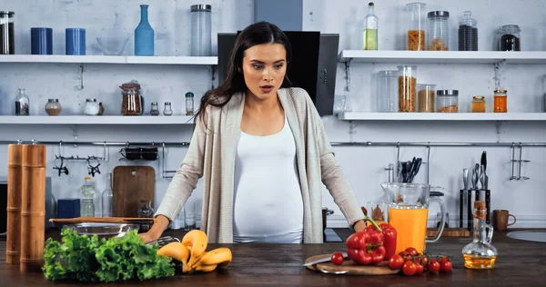 Aufgeregte Schwangere Blickt Auf Frische Zutaten Auf Küchentisch — Stockfoto