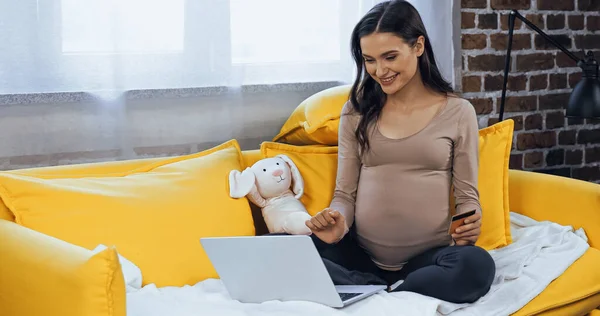 Happy Pregnant Woman Credit Card Using Laptop Soft Toy Couch — Stock Photo, Image