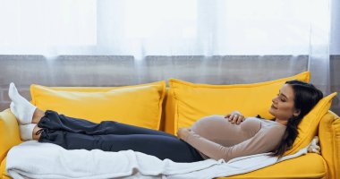 Hamile kadın evdeki kanepede dinleniyor. 