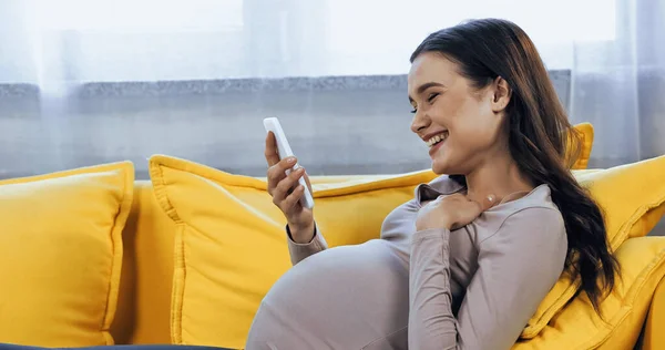 Smiling Pregnant Woman Holding Smartphone Bright Yellow Couch — Stock Photo, Image