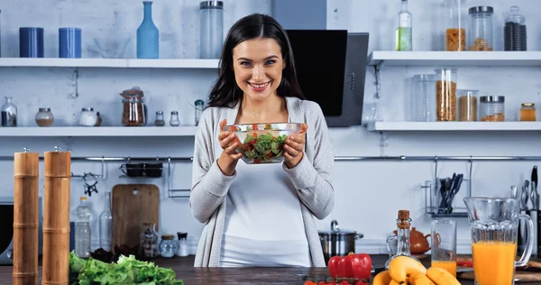 Mulher Sorridente Segurando Salada Fresca Perto Ingredientes Crus Cozinha — Fotografia de Stock