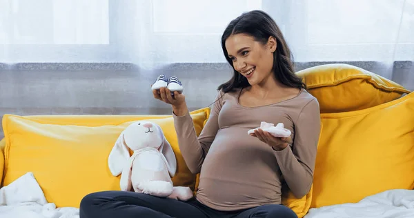Smiling Pregnant Woman Looking Baby Booties Soft Toy Couch — Stock Photo, Image