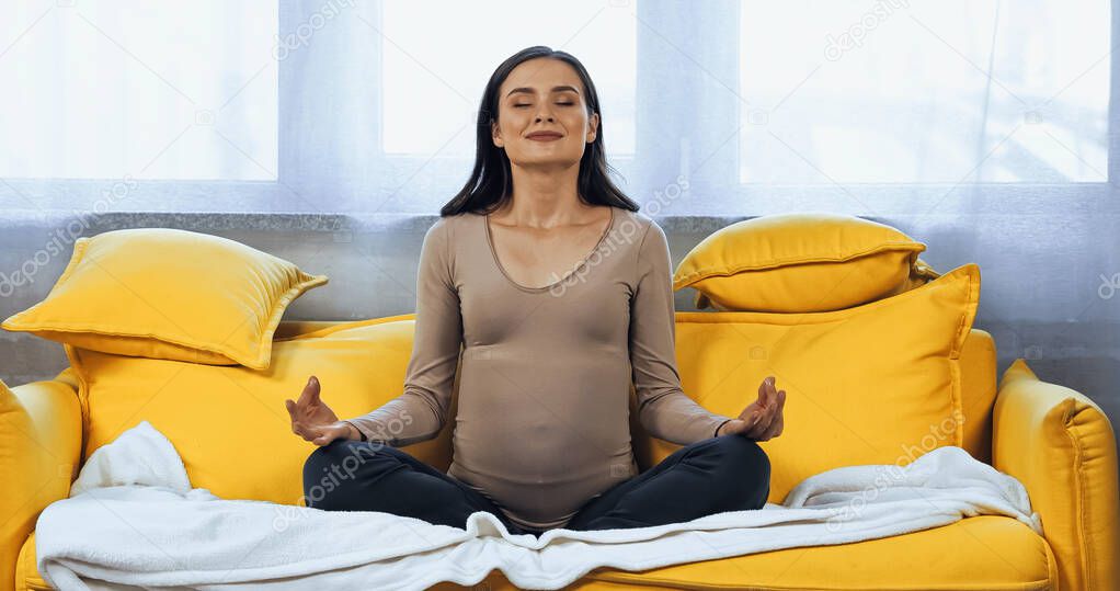 Smiling pregnant woman meditating with closed eyes on couch 