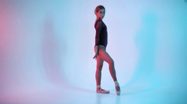 Genç balerin dans ediyor ve mavi arka planda kameraya bakıyor.