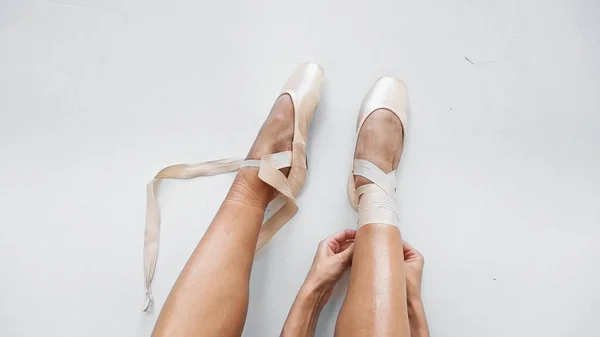 Top view of ballerina tying pointe shoes on white background