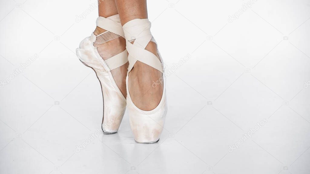 partial view of ballerina in pointe shoes dancing on white