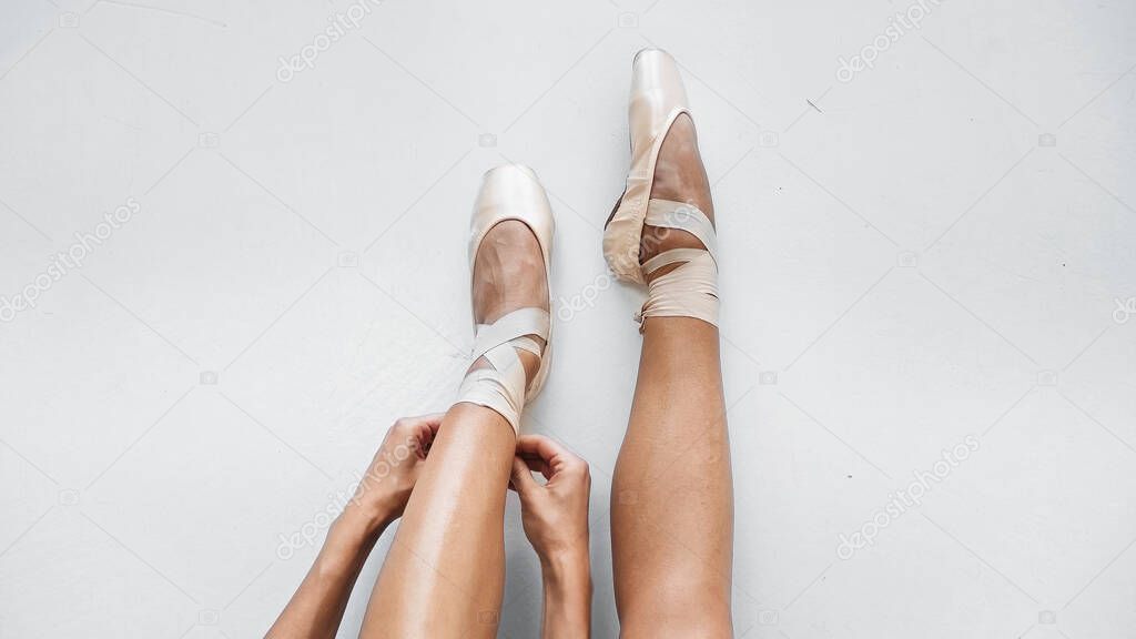 partial view of ballerina tying pointe shoes on white background