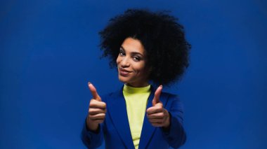 Gülümseyen Afro-Amerikan kadın mavi üzerinde parmaklarını gösteriyor. 