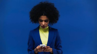 Genç Afro-Amerikan kadın mavi üzerinde izole akıllı telefon kullanıyor.