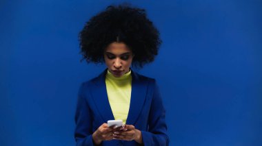 Young african american woman using smartphone isolated on blue clipart