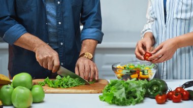 Mutfakta taze salata hazırlayan yaşlı çiftin kırpılmış görüntüsü.