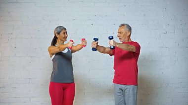 senior interracial couple looking at each other while exercising with dumbbells  clipart