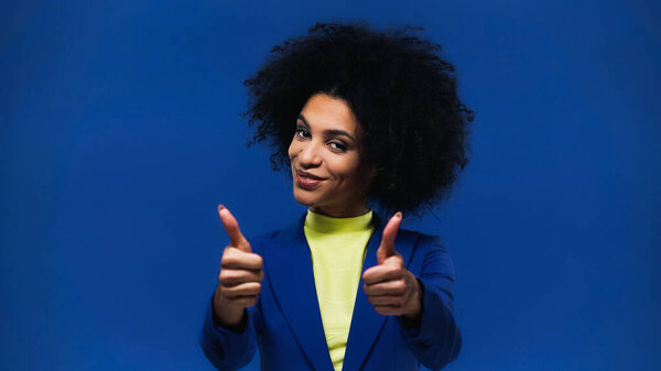 Smiling african american woman showing thumbs up isolated on blue 