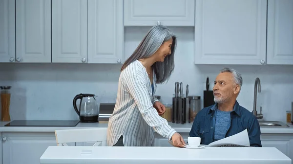快乐的灰白头发的亚洲女人在厨房为年长的丈夫端咖啡 — 图库照片