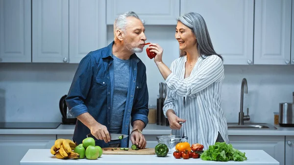 Happy Asian Woman Feeding Husband Bell Pepper While Preparing Breakfast — Stock Photo, Image