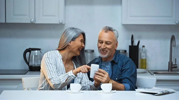 Laughing Asian Woman Pointing Finger Smartphone Smiling Husband — Stock Photo, Image