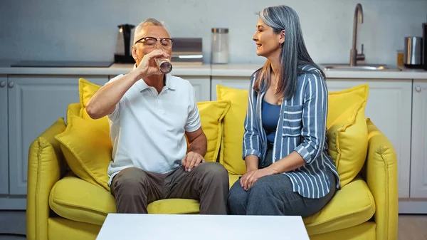 Elderly Man Drinking Water Smiling Asian Wife Sitting Couch Home — Stock Photo, Image