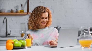 Mutfakta online alışveriş yaparken elinde kredi kartı tutan mutlu genç bir kadın. 
