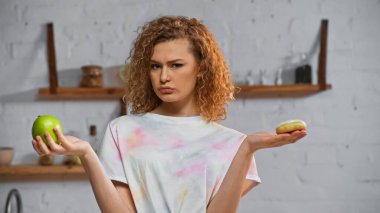 curly young woman choosing between apple  and donut clipart