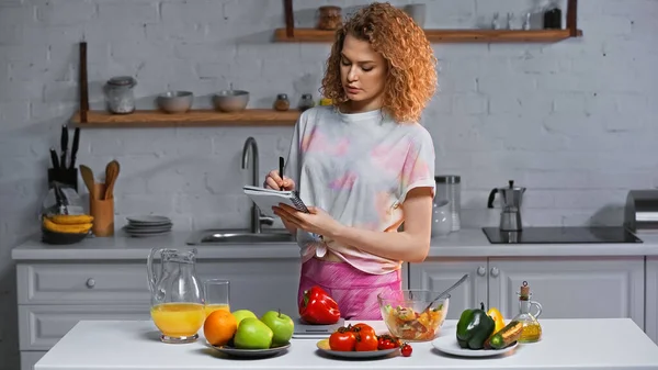 Curly Woman Notebook Weighing Bell Pepper Vegetables Orange Juice Table — Stock Photo, Image