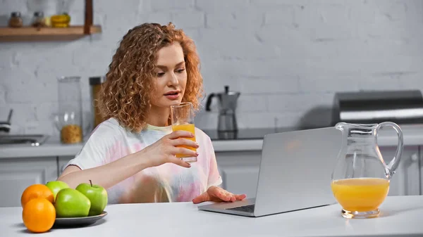 Curly Young Woman Looking Laptop While Holding Glass Orange Juice — Stock Photo, Image