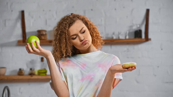 curly young woman choosing between donut and apple  