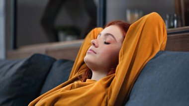 Red haired girl sitting with closed eyes on couch  clipart