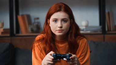 KYIV, UKRAINE - 8 Kasım 2019: Kızıl saçlı genç elinde joystick ile kameraya bakıyor 