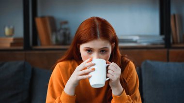 Süveter giyen, elinde çay tutan bir genç. 