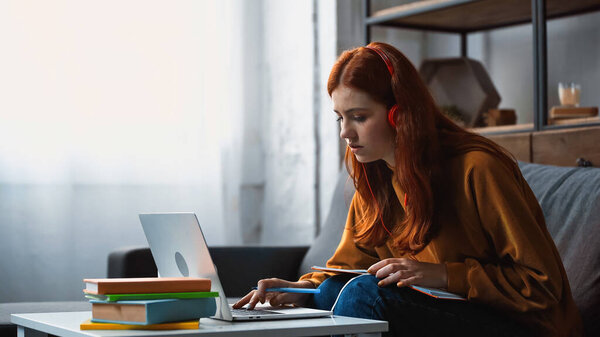 Student in headphones using laptop near books on blurred foreground 