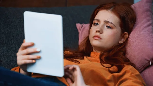 Red haired girl using digital tablet on blurred foreground at home