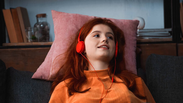 Smiling girl listening music in headphones on pillows 