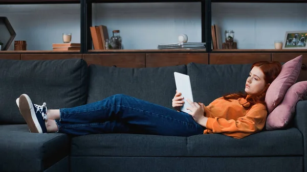 Triste Menina Cabelos Vermelhos Usando Tablet Digital Enquanto Deitado Sofá — Fotografia de Stock